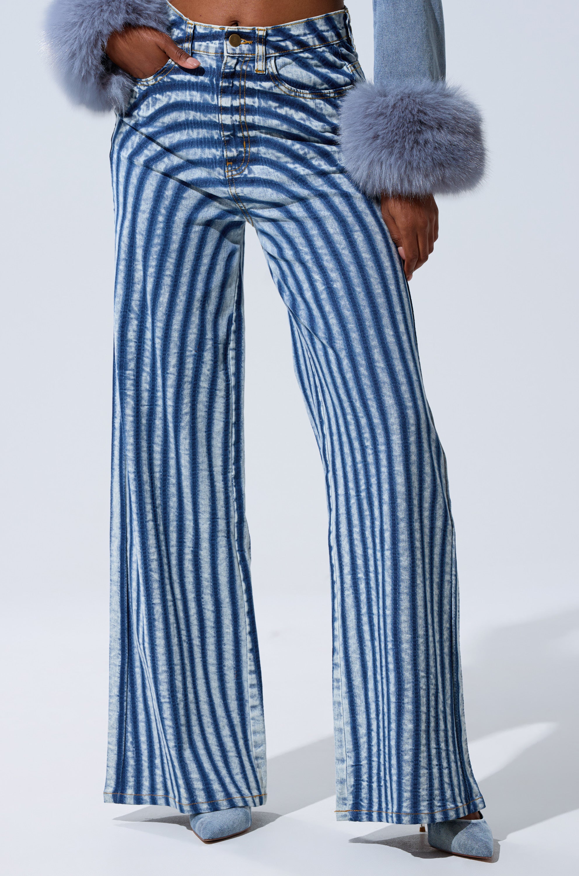 Someone stands against a plain light background wearing LETS GET CRAZY STRIPE WIDE LEG DENIM in blue and white, a light blue top with large, fluffy gray cuffs, and gray pointed-toe shoes.