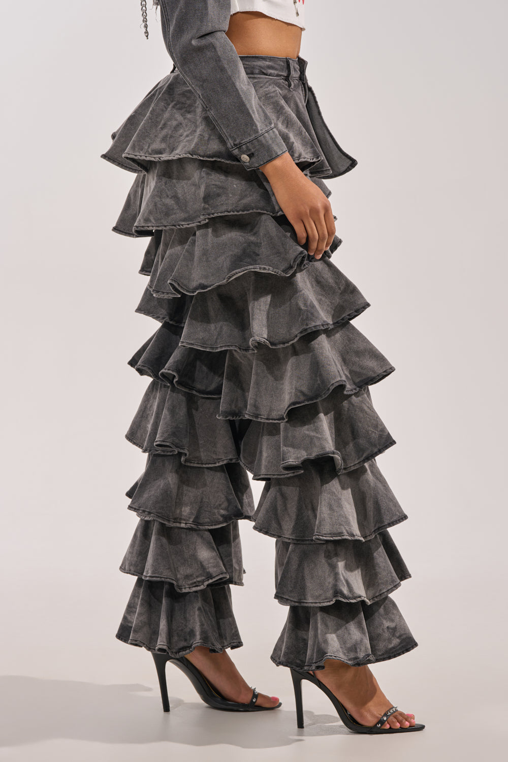 A person wearing LOOK THIS WAY RUFFLE DENIM PANT with layered ruffles, paired with a matching ruffled jacket and high-heeled sandals. The side-view photo is set against a plain background. 2
