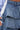 Close-up of a person wearing the LOOK THIS WAY RUFFLE DENIM PANT with two tiered layers, paired with a blue and white striped long sleeve shirt. The person's hand is partially visible to the left.