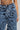 A person is wearing the TOUCH ME DISTRESSED DENIM PANT with frayed, heavily distressed texture and shredded detailing. The high-rise waist of these jeans slightly reveals a tattoo displaying the numbers 