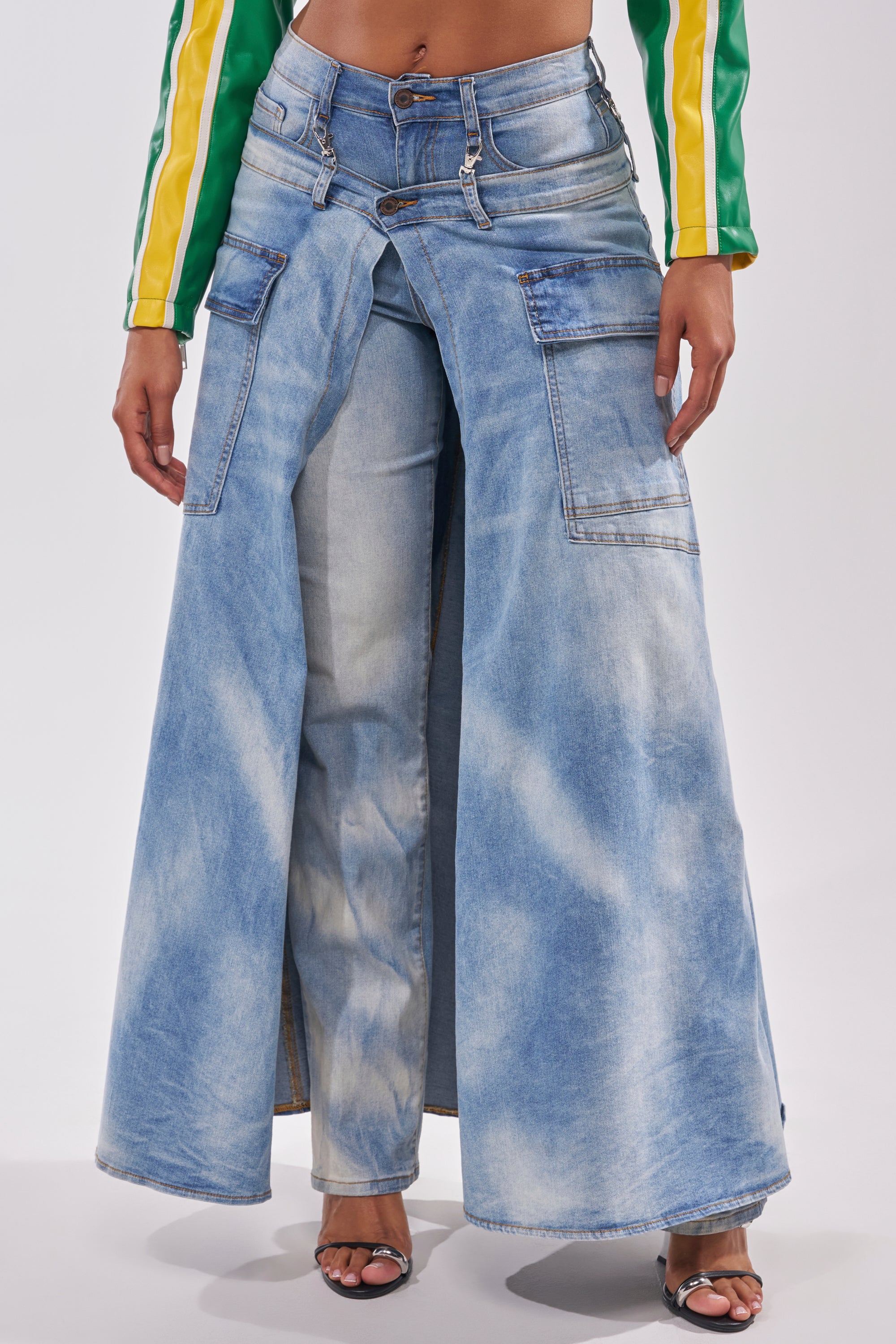 Wearing the OVER IT DENIM PANT, featuring wide, skirt-like outer legs over classic jeans, channels deconstructed street style when paired with open-toe heels and a green and yellow long-sleeve top. 1