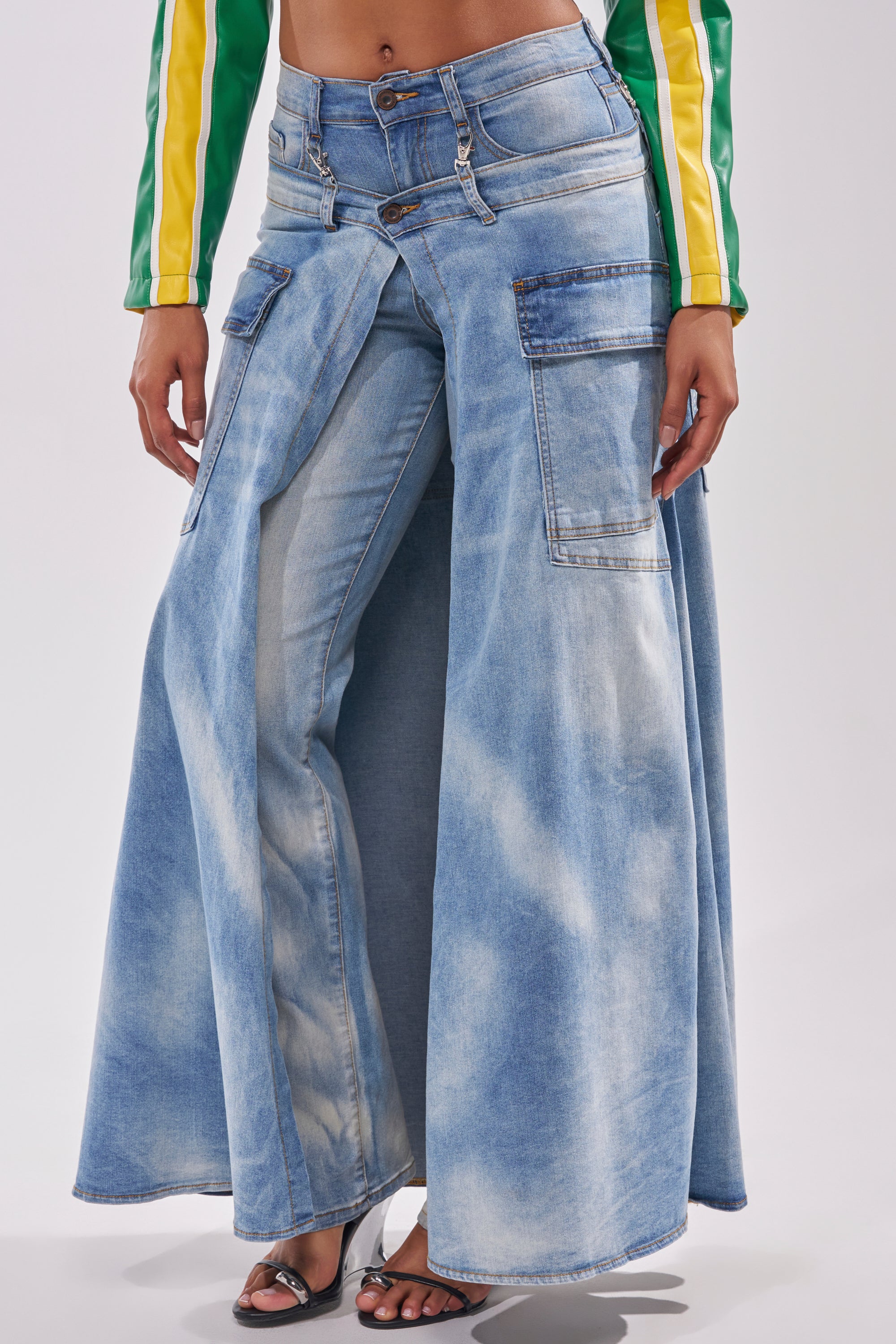 A person wears the OVER IT DENIM PANT, a light blue street-style jean with shorts over wide, skirt-like legs, paired with a green and yellow long-sleeve top and open-toe heels. 2