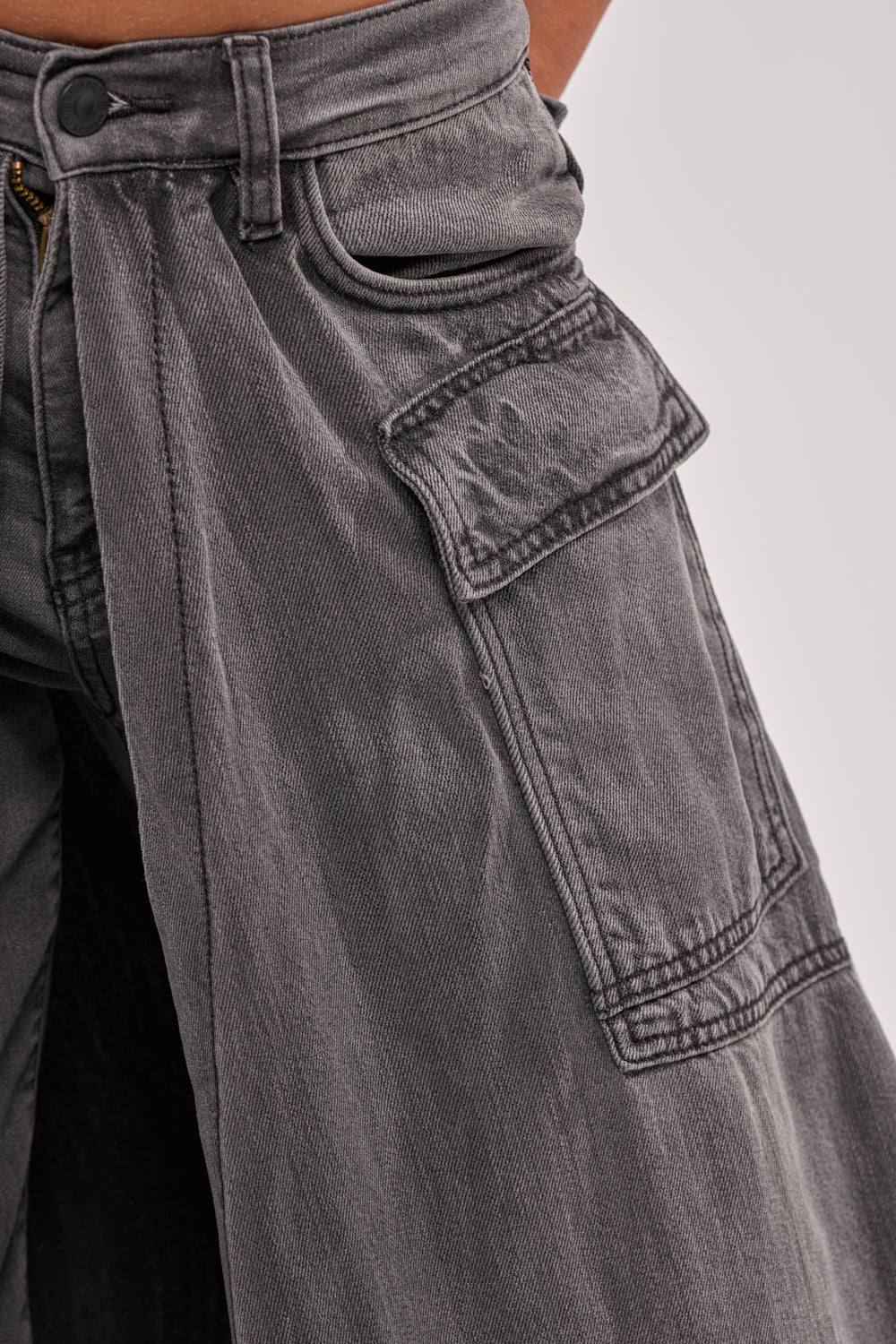 Close-up of a person wearing the MIXED EMOTIONS DENIM PANT—high-waisted, loose-fitting straight-leg jeans featuring a large thigh flap pocket, slightly worn fabric, and visible stitching details. 9