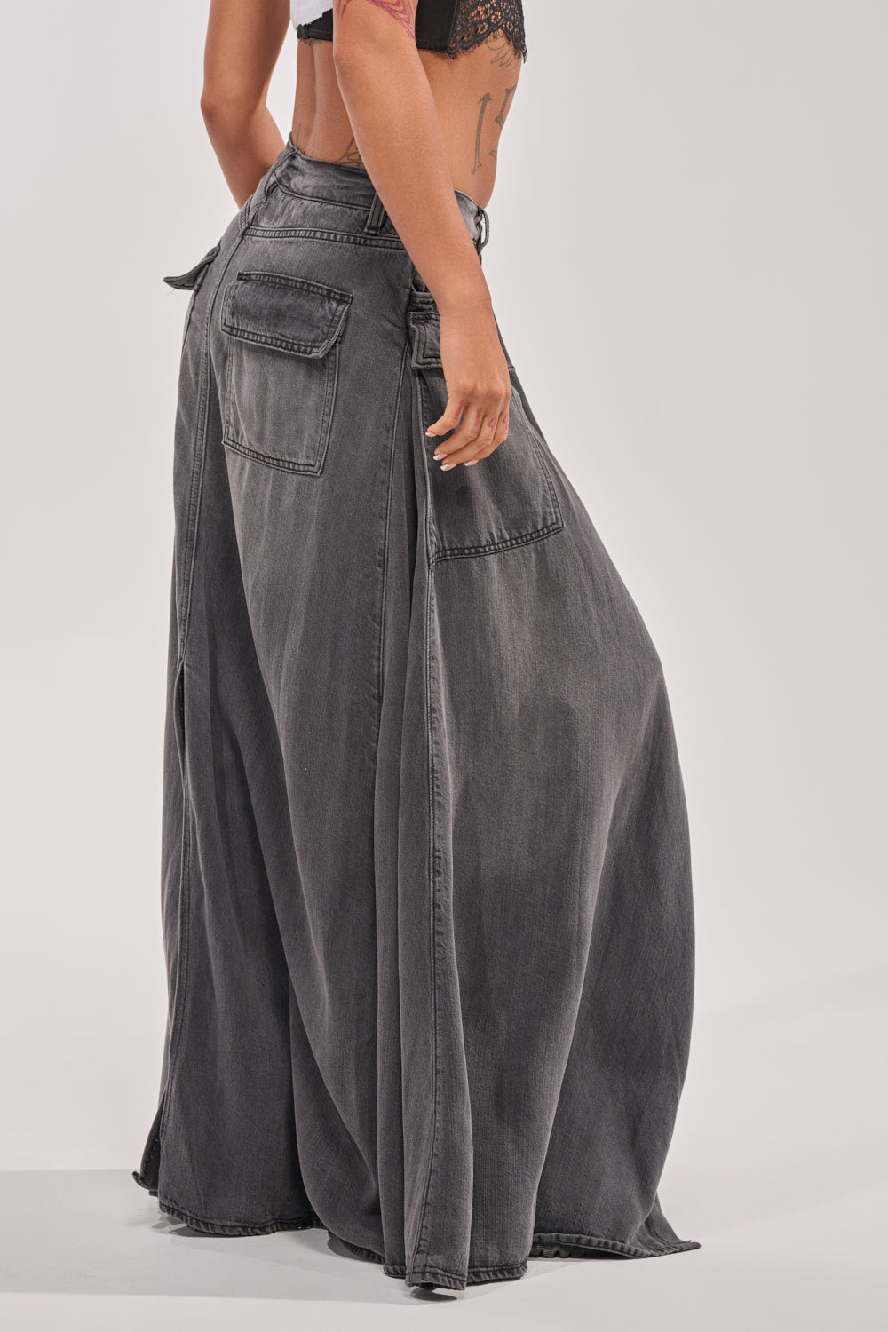 A person is seen from behind wearing the MIXED EMOTIONS DENIM PANT—wide-leg, high-waisted faded black jeans with large back pockets and exposed seams—styled with a black cropped top. 3