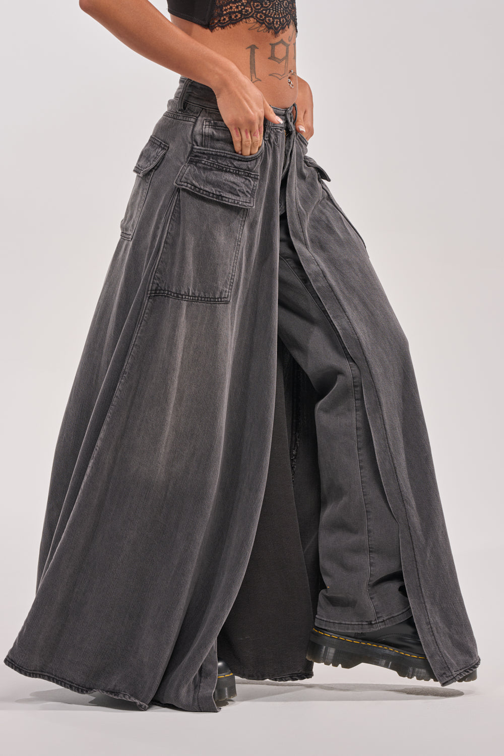 Model wearing MIXED EMOTIONS DENIM PANT—wide-leg, dark grey cargo jeans with large pockets and straight-leg fit, cropped at the waist. Styled with black platform boots and set against a plain light background. 4