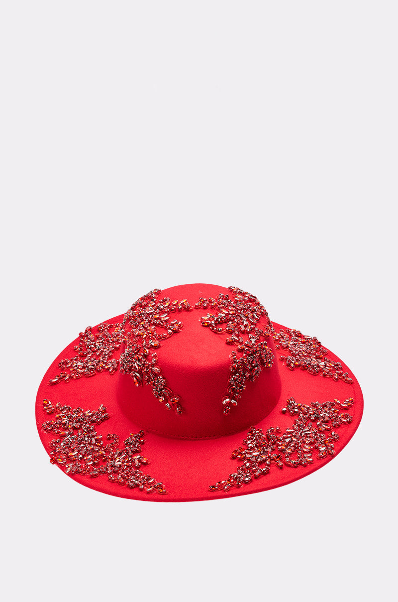 The TALK OF THE TOWN BRIM HAT is a bright red wide brim hat adorned with clusters of red and gold beads, sequins, and rhinestone embellishments, shown against a plain light background. 1