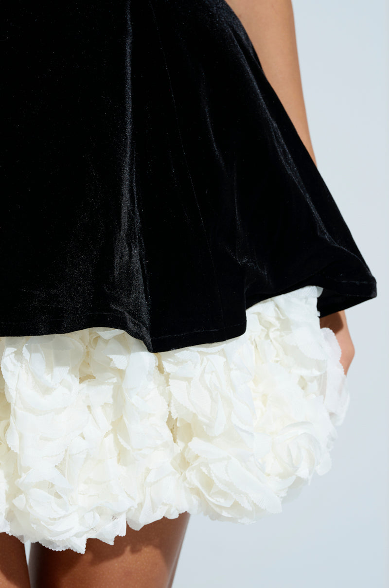 Close-up of the CHARLOTTE LAYERED VELVET MINI DRESS, showcasing a black velvet top with layered ruffles resembling roses or petals on a white textured floral bottom. The skirt's striking texture and color contrasts are highlighted in the image.