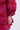 A person’s arm and hand rest by their side, wearing the AMALIA TIE NECK TRENCH—a textured red and pink brocade-patterned garment with puffy sleeves—against a light, plain background.
