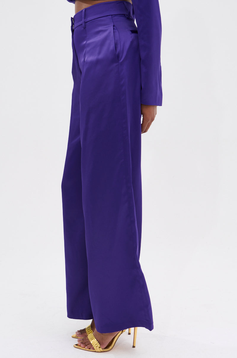 A person wears the SAY YOU LOVE ME SATIN TROUSER, featuring a wide leg silhouette and high-rise fit, paired with gold high heels against a plain white background.