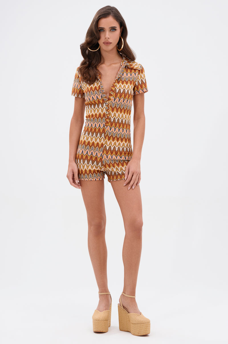 A woman stands against a white background wearing the RYLEE ABSTRACT PRINT COLLARED ROMPER IN BROWN, featuring short sleeves and zigzag abstract print, paired with beige platform heels and large hoop earrings.