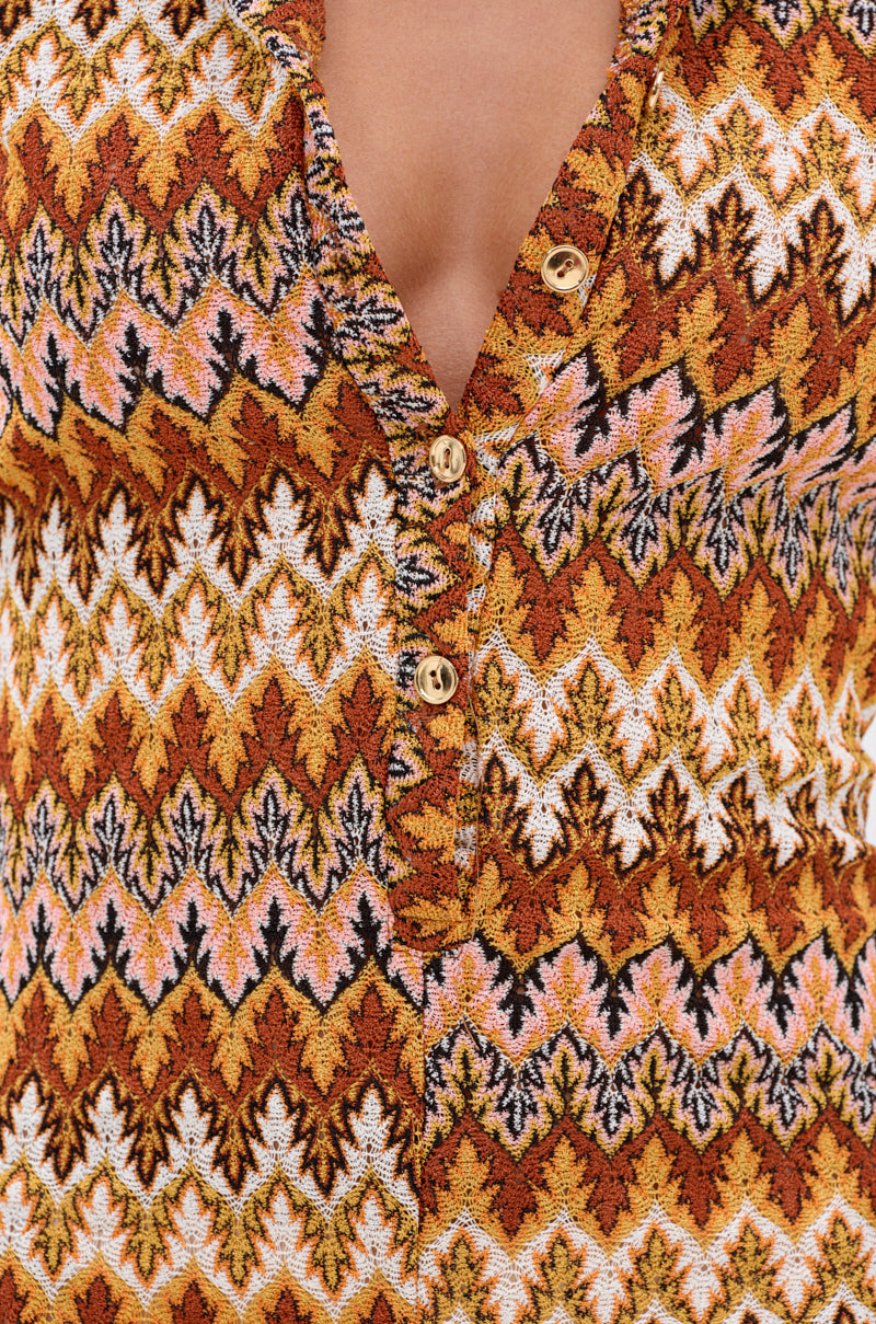 Close-up of the RYLEE Abstract Print Collared Romper in Brown, featuring zigzag patterns in brown, orange, white, and black. The romper is partially unbuttoned to show a v-shaped neckline with three visible buttons.