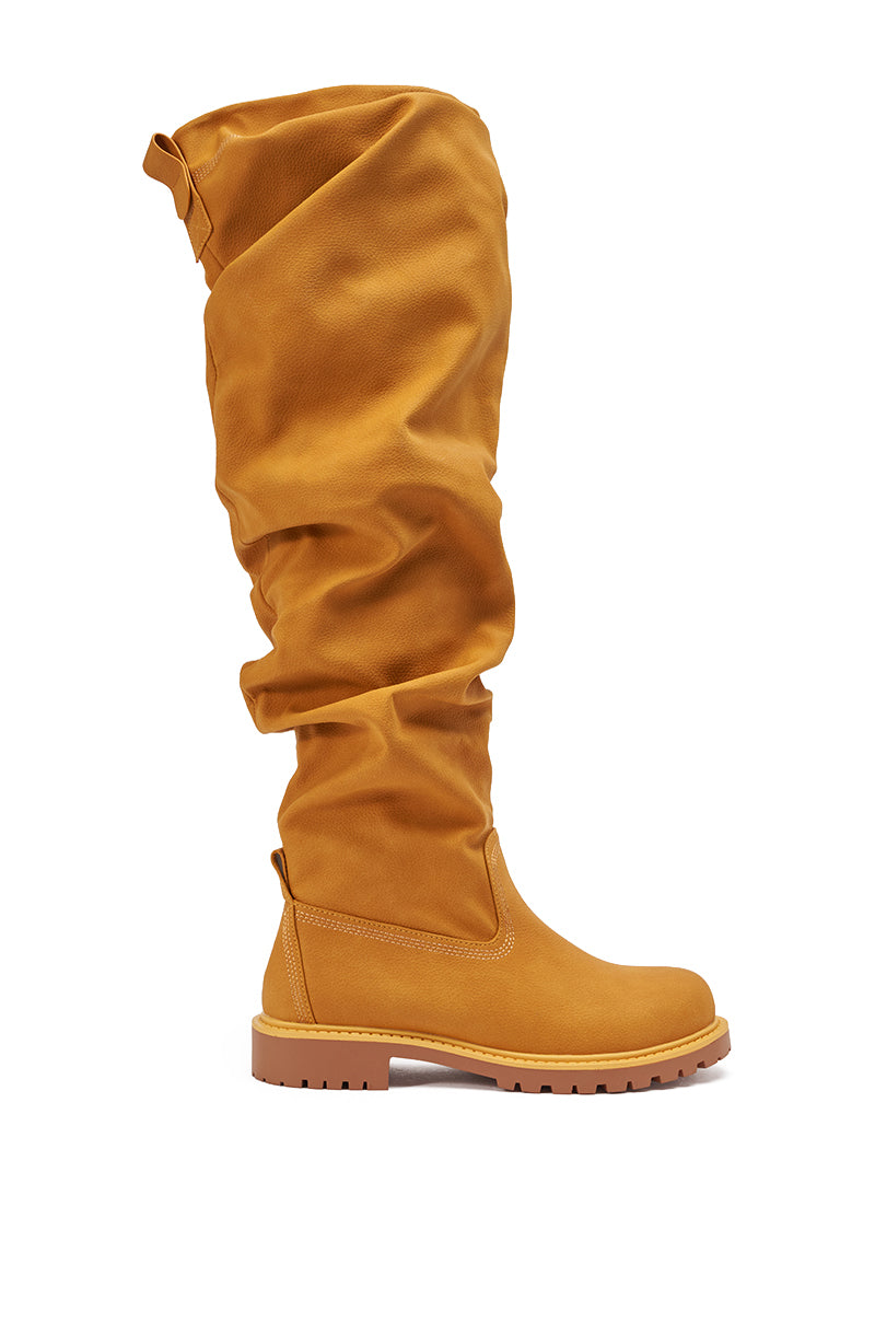 The AZALEA WANG ARDIS TAN RUCHED FLAT BOOT, a single tan knee-high boot with a soft ruched design, rugged thick rubber sole, and rounded toe, stands upright against a white background. 3
