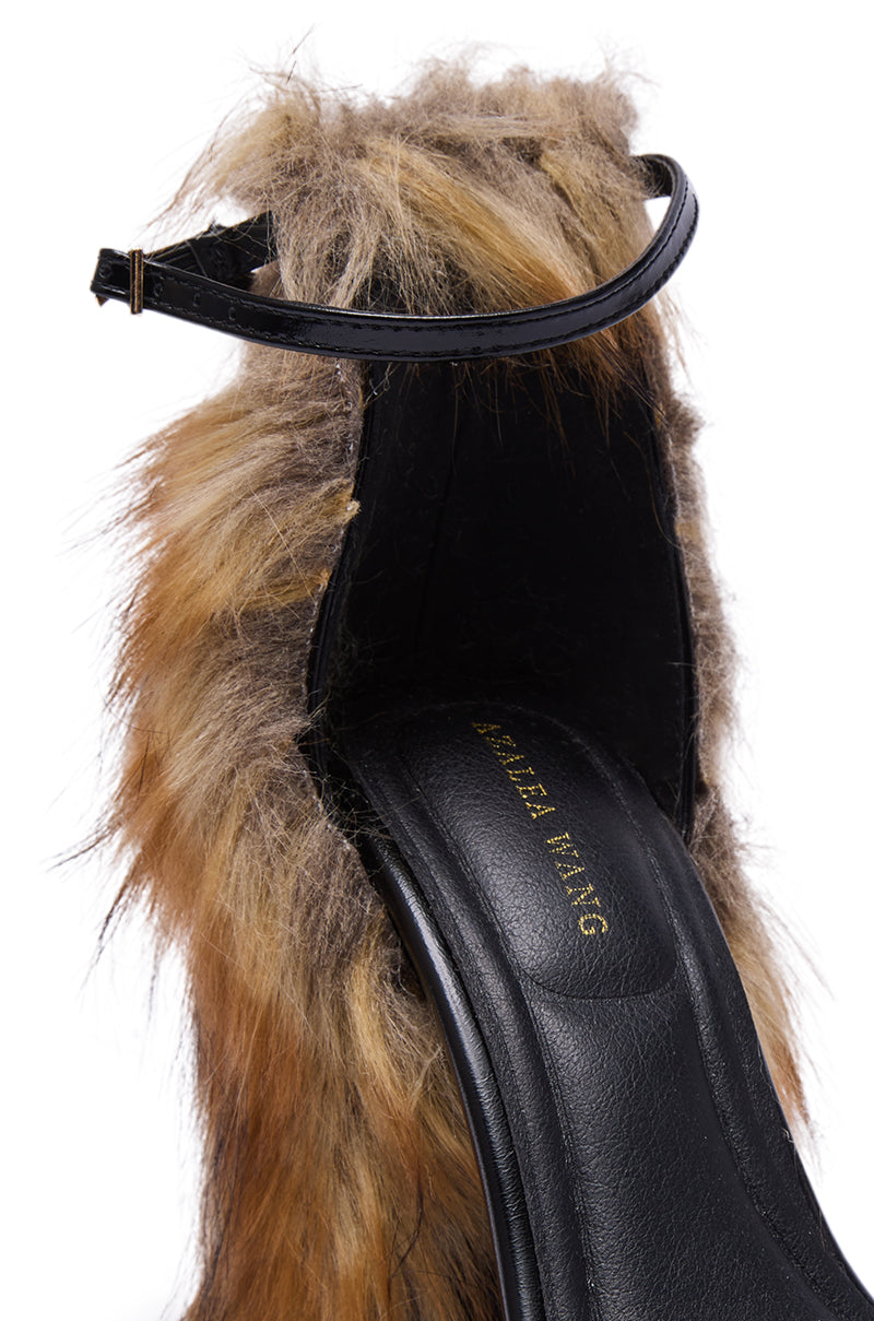 The AZALEA WANG ARETTE BLACK SANDAL WITH BROWN FUR features a chunky high heel, black leather sole with gold lettering, ankle strap, and a unique textured look with brown and tan faux fur covering.