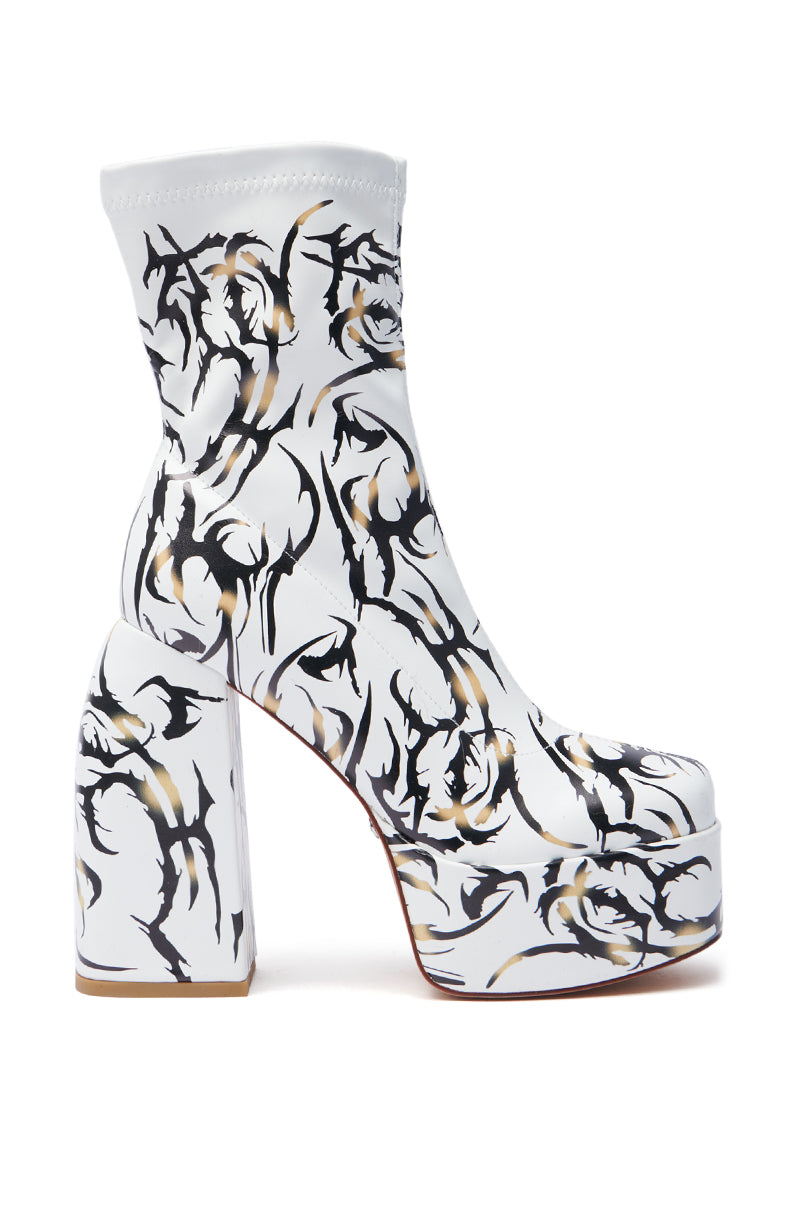 The AZALEA WANG ARIADNE WHITE CHUNKY BOOTIE features a white platform sole with an artistic black and gold brushstroke design, reminiscent of tattoo art. It includes a high block heel and a seamless finish.