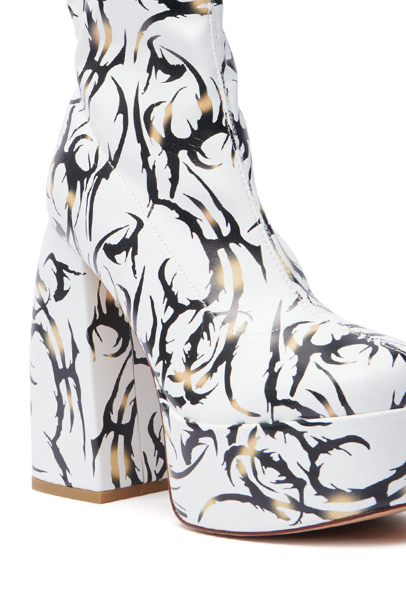 The AZALEA WANG ARIADNE WHITE CHUNKY BOOTIE features a tattoo-inspired black and tan pattern, showcased on a pristine background with its stylish chunky heel and platform sole adding an edgy vibe.
