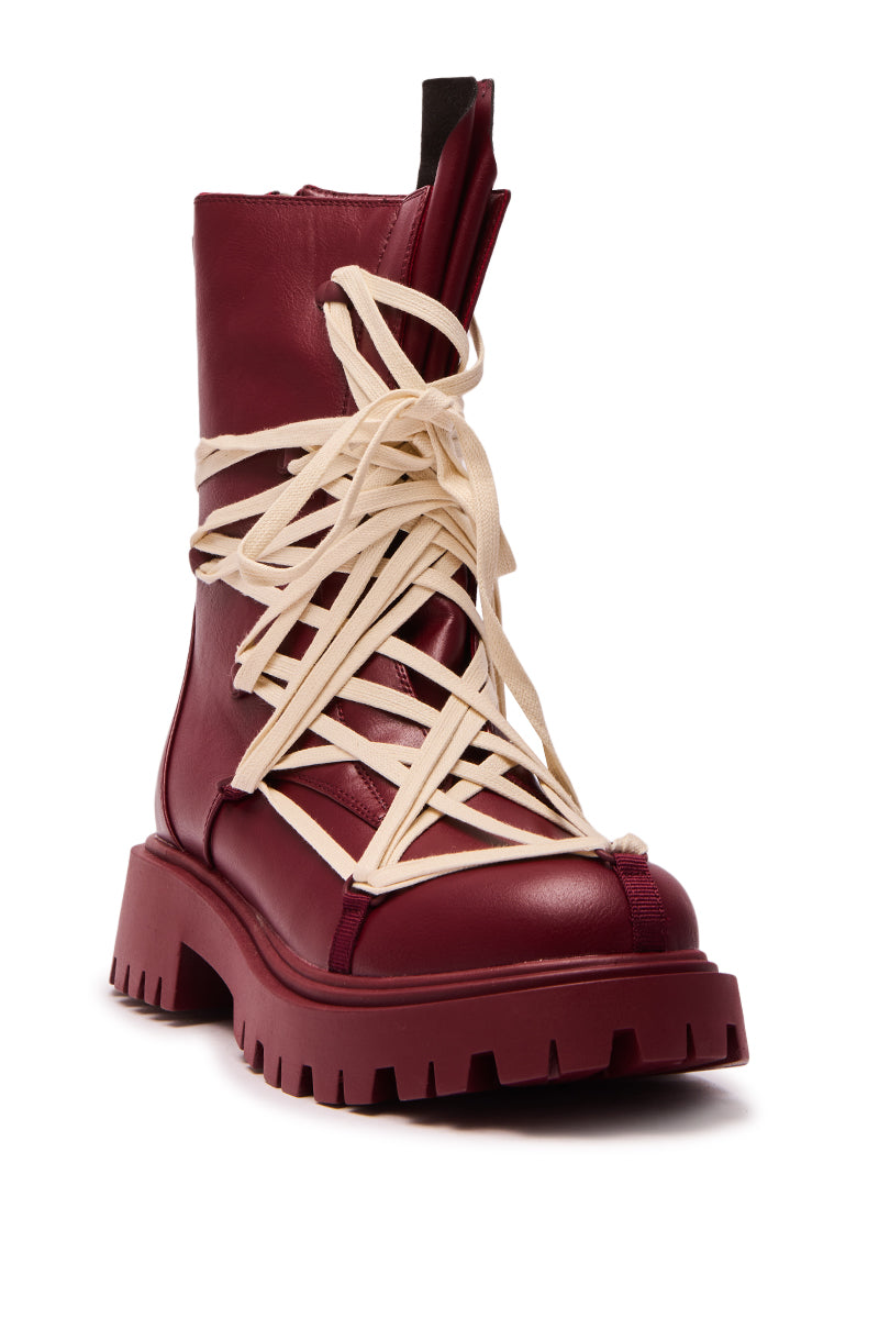 The AZALEA WANG ARJUN BURGUNDY LACE DETAIL BOOTIE is a chunky faux leather combat boot with a thick tread sole, featuring standout oversized cream laces dramatically crisscrossed around the front and sides.