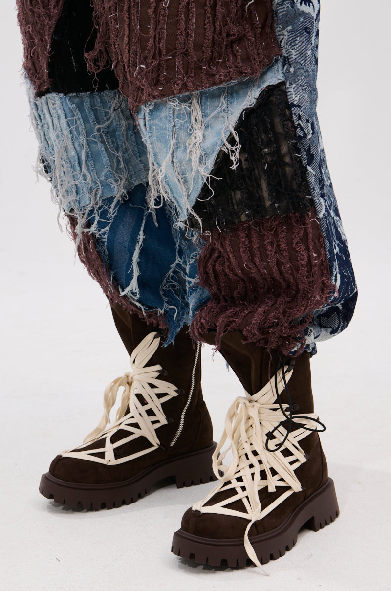 A close-up of a person wearing the AZALEA WANG ARJUN CHOCOLATE LACE BOOTIE with chunky heels and thick white laces, styled with distressed patchwork jeans in frayed blue and maroon denim.