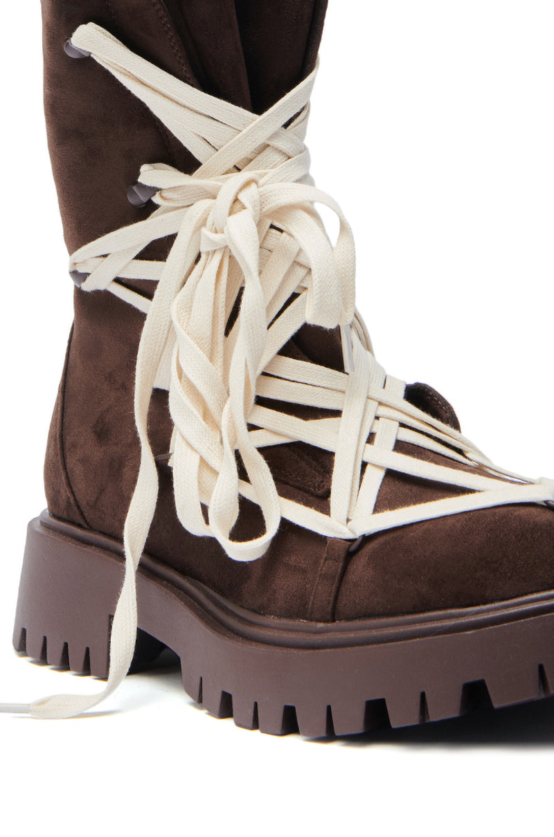 A close-up of the AZALEA WANG ARJUN CHOCOLATE LACE BOOTIE, a faux suede combat boot with thick, rugged soles and wide white laces wrapped around the ankle and tied in a large knot.