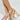Close-up of someone wearing AZALEA WANG ARLETH GOLD SANDAL with gold platform and chunky block heels, adorned with white bead straps and colorful shell embellishments, elegantly positioned against a neutral background.