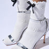 A person wearing white socks adorned with floral designs and black ribbon bows is paired with the AZALEA WANG ARNALDO STILETTO SANDAL in metallic silver. These sandals showcase a sleek stiletto heel and delicate ankle straps, enhanced by a Comfort Cushion insole for luxurious support.