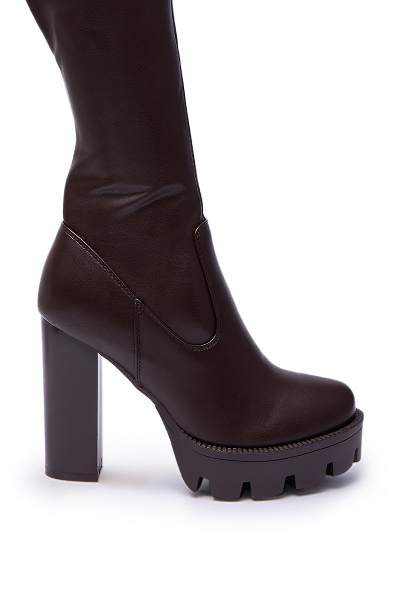 A close-up of the AZALEA WANG ASHLAND CHOCOLATE STRETCH PU CHUNKY THIGH-HIGH BOOT featuring a chunky heel and thick treaded sole, displayed against a white background.