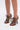 A person wears the AZALEA WANG ASHLIE COLOR BLOCKED SNAKE SANDAL with stiletto heels and open toes, featuring a brown faux leather snakeskin pattern, while standing on a white background.