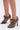 A person wears the AZALEA WANG ASHLIE Color Blocked Snake Sandal—brown, lace-up, stiletto heel peep-toe shoes—standing on a white background.