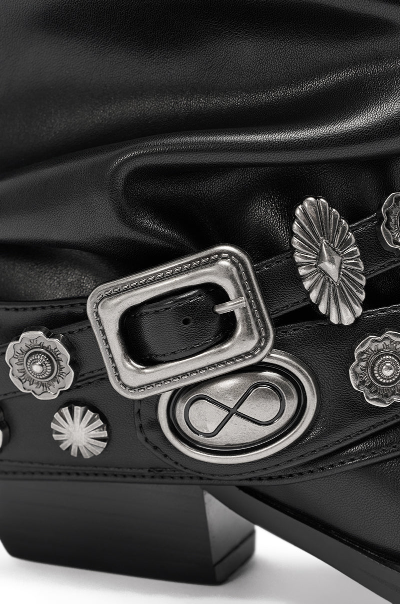 Close-up of the AZALEA WANG Ashraf Black PU Silver Hardware Western Bootie, featuring a strap with silver buckle, floral and starburst shapes, an engraved infinity symbol on an oval plate, and a chunky modern heel.