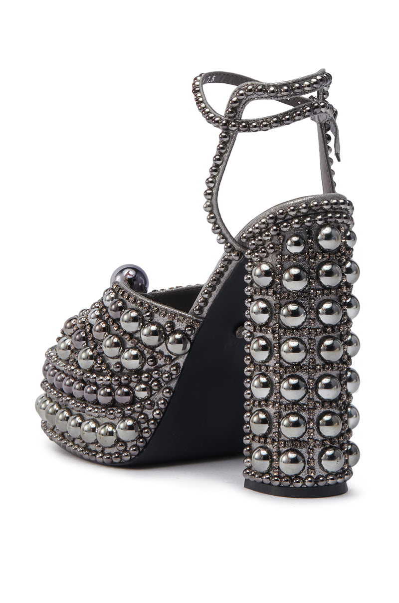 The AZALEA WANG ASTRELLA HEMATITE EMBELLISHED SANDAL features a high block heel, chunky platform, ankle strap, and rounded toe, all adorned with rows of shiny silver studs and beads for a bold, textured look.