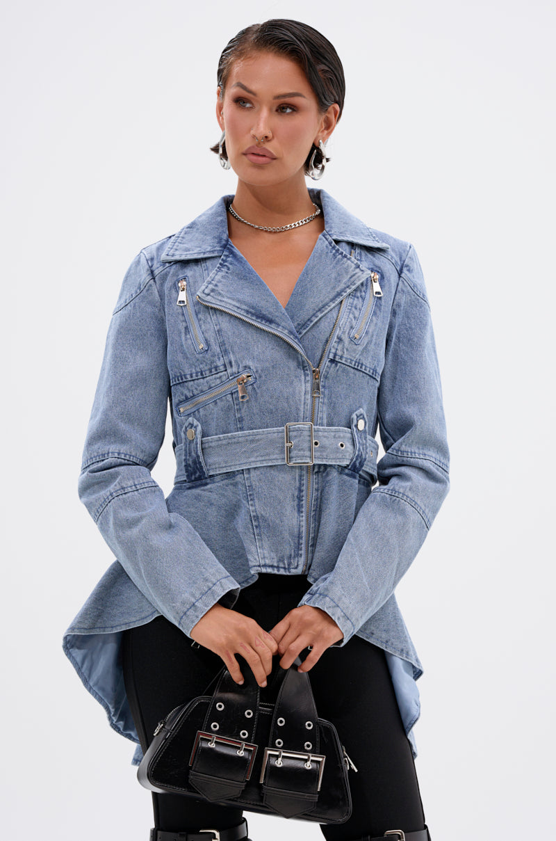Wearing the ASTRO HIGH LOW DENIM JACKET with a belted waist, black leggings, and a small black handbag, this person’s look is completed with short slicked-back hair, silver earrings, and a chain necklace.