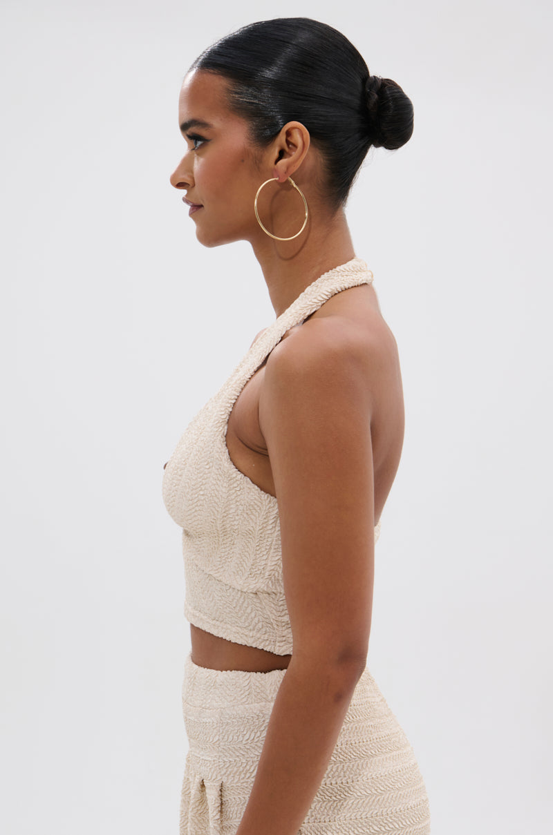 A dark-haired woman with a sleek bun and large hoop earrings models the HOLLYWOOD SLINKY TEXTURED BRALETTE with matching high-waisted bottoms, standing in profile against a plain white background, exuding boho flair.