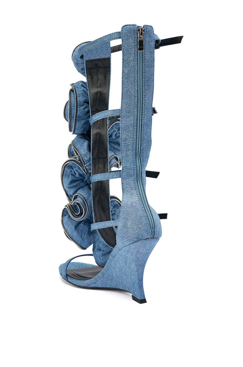 The AZALEA WANG ATLANTIC DENIM GLADIATOR WEDGE is a knee-high sandal with gladiator straps, ruffle details, zipper accents, open toe, and wedge heel, displayed against a white background.