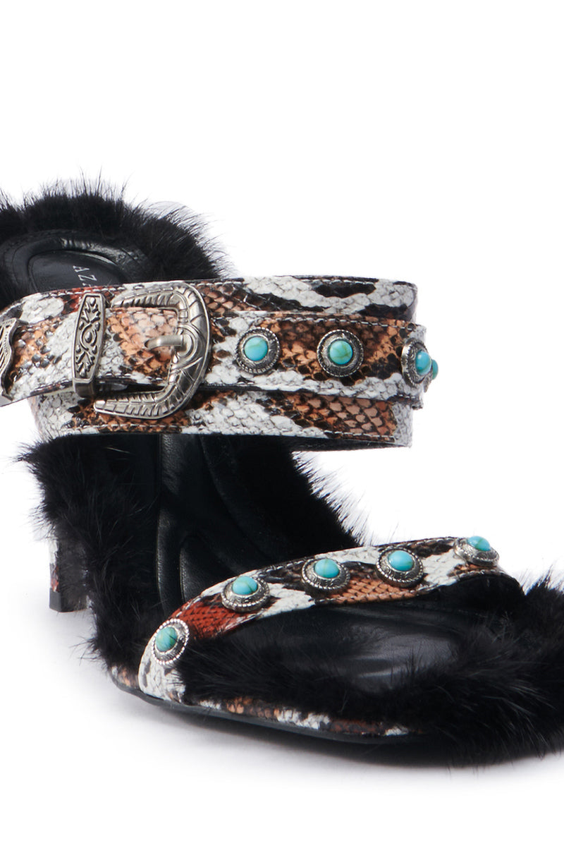 The AZALEA WANG AUGER BROWN SANDAL is a chic high-heeled shoe with a striking snakeskin pattern, embellished with turquoise studs and silver buckles. It features black fluffy trim and is made from vegan leather, providing a bold fashion statement.
