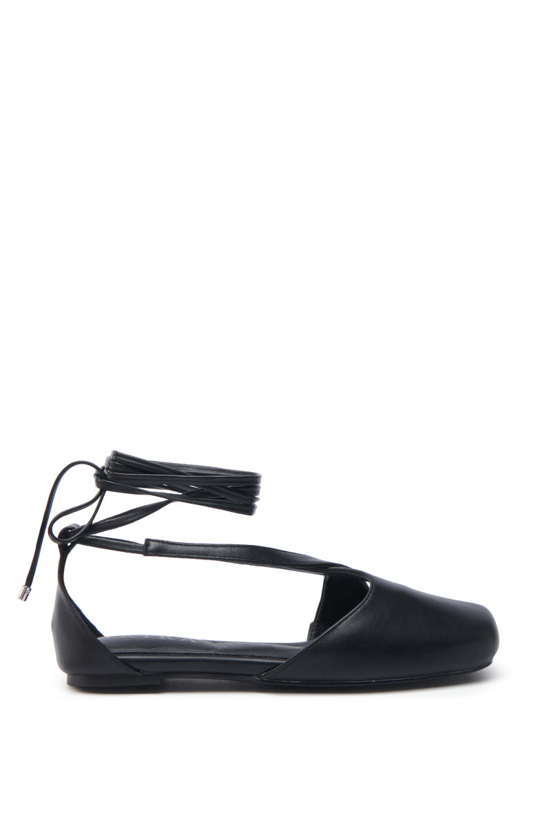 The AKIRA AULORA Black Flat Sandal features a sleek design with peep toe, thin ankle wrap laces, vegan leather construction, and cushioned insole for comfort, shown in profile against a white background.