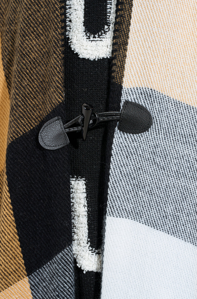 Close-up of the AURETA NEW PLAID MAXI PONCHO featuring a horn toggle button. The poncho showcases an ultra-soft knit fabric in tan, white, black, and gray. The black toggle is fastened with matching loops, beautifully highlighting the woven threads' texture. 5