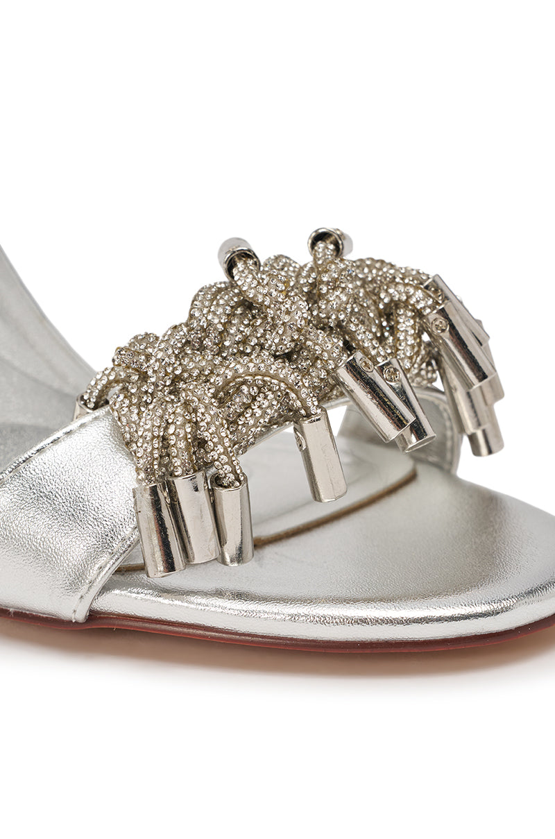 Close-up of the AKIRA GOLD AURIELLE Silver Rhinestone Embellished Stiletto Sandal, featuring metallic silver straps with braided detailing, shiny beaded accents, a rhinestone ankle cuff, and a sleek stiletto heel. 6