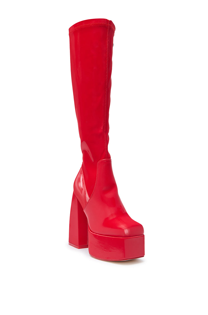 The AZALEA WANG AURON RED LIQUID LUXE PLATFORM BOOT is a shiny, bright red knee-high boot with a chunky high heel and rounded toe, crafted from glossy faux patent leather.