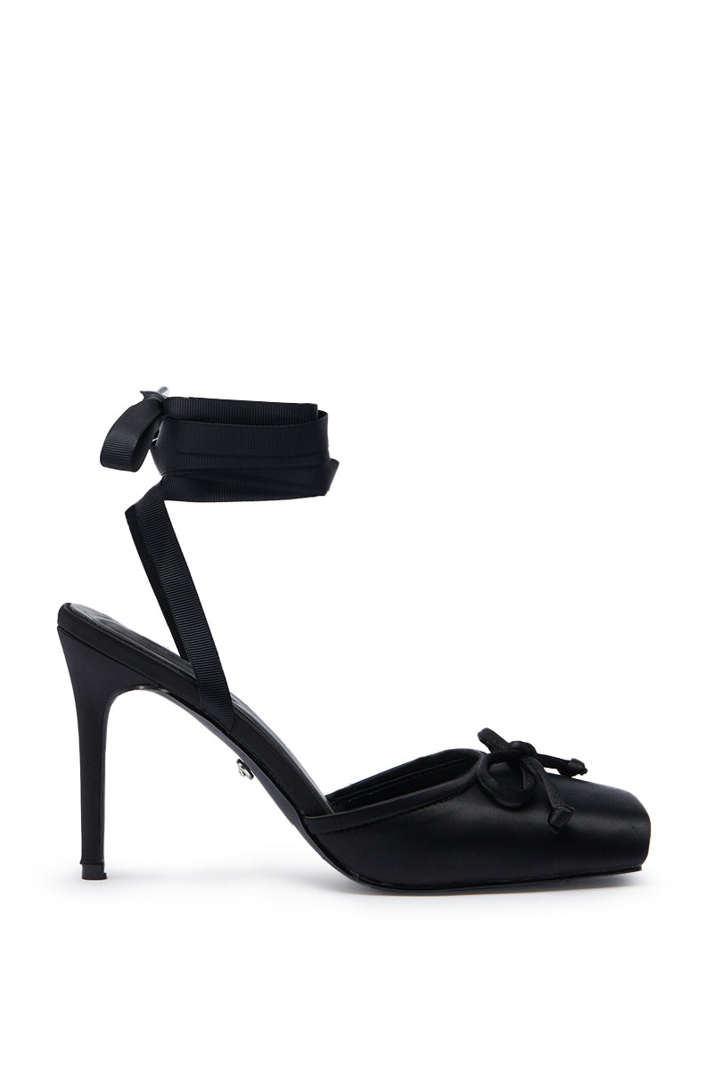 The AZALEA WANG AURORIA BLACK BALLET PLATFORM PUMP features a black satin upper, ankle wrap-around ribbon, and a decorative front bow, shown on a white background.