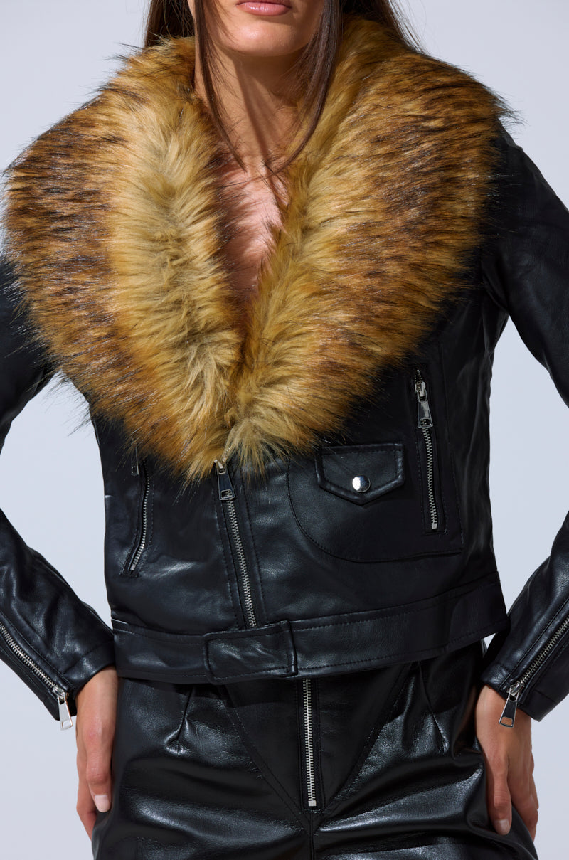Modeling the AUSSY FUR COLLAR MOTO, a black faux leather jacket with a bold, fluffy brown fur collar and matching pants—a chic statement in women's outerwear—she strikes a confident pose with hands on hips.