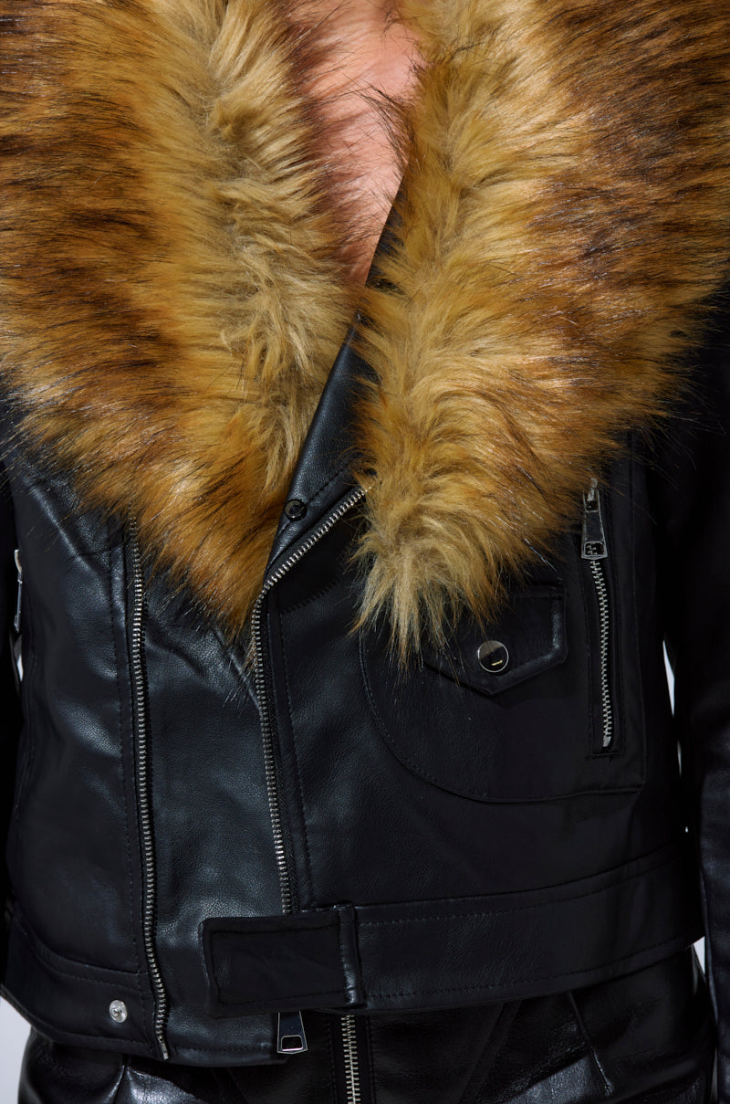 The AUSSY FUR COLLAR MOTO is a black faux leather jacket for women, featuring a large brown faux fur collar, zip details, a pocket, and a belt. Shown in close-up; model’s face not visible.
