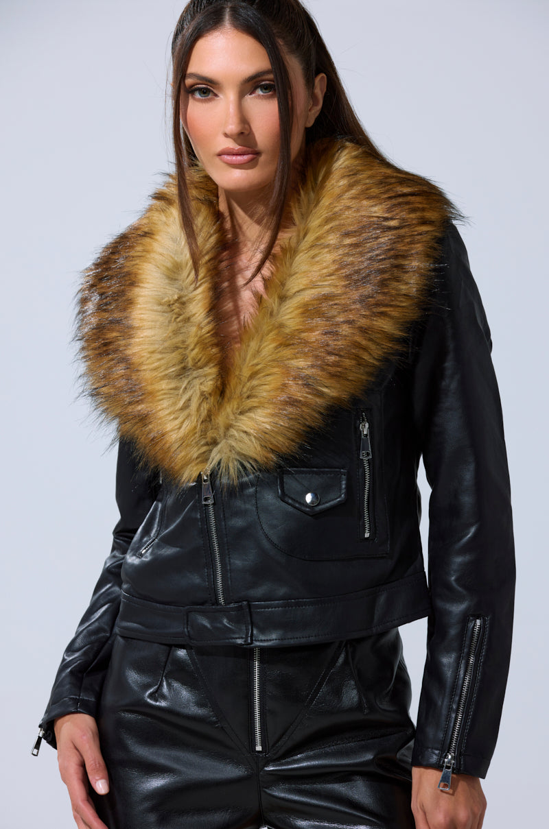A woman models the AUSSY FUR COLLAR MOTO jacket, featuring a chic faux leather design with a large brown fur collar, paired with matching black leather pants against a plain light background.