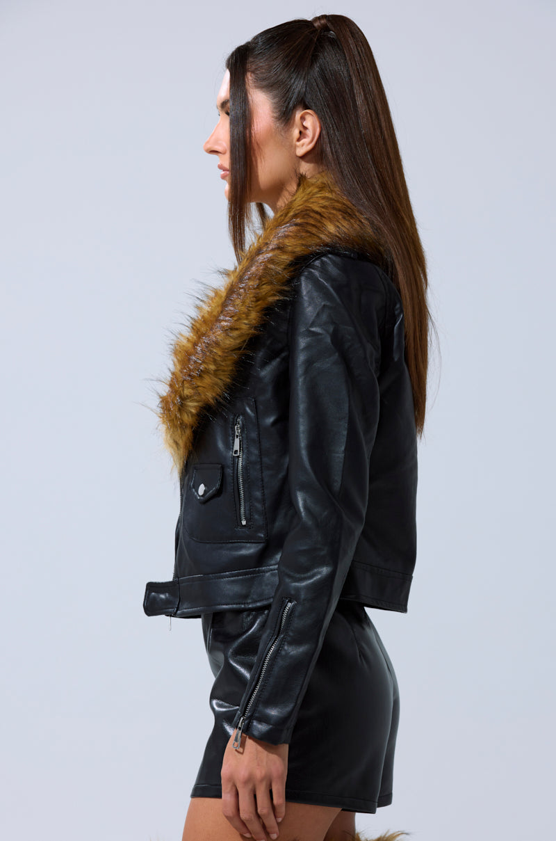 A woman with long straight hair models the AUSSY FUR COLLAR MOTO—a black faux leather jacket with a brown fur collar—paired with matching shorts, posing in profile against a light background to showcase this chic outerwear.