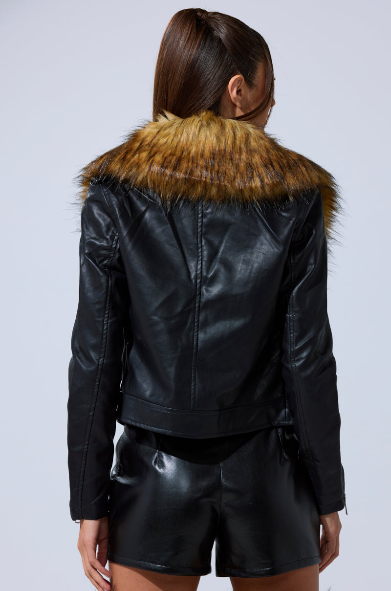 A woman with long, straight brown hair models the AUSSY FUR COLLAR MOTO, a black faux leather moto jacket with a large brown fur collar and matching shorts, shown from the back against a plain light background.
