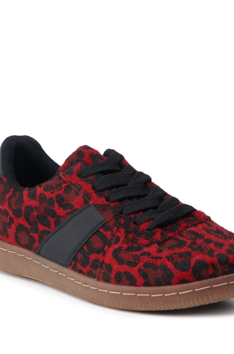 The AZALEA WANG AVENGER RED LEOPARD SNEAKER showcases an eye-catching red and black leopard-print pattern complemented by black laces. It features a brown rubber sole, a sleek black side stripe, and a soft, cushioned collar for added comfort. The faux pony hair texture adds an extra layer of luxury to this lace-up vamp design.