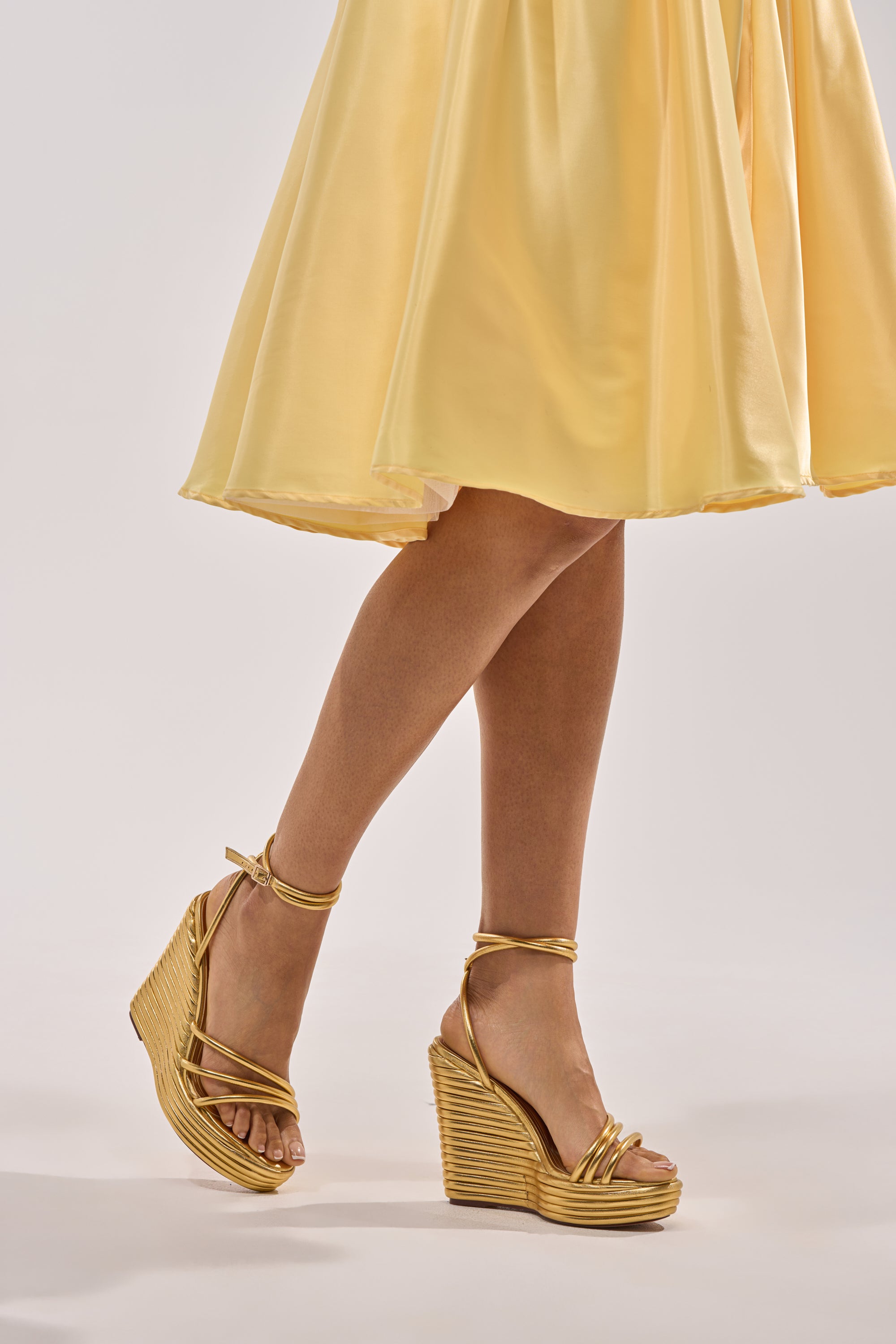 A person wearing a yellow, knee-length skirt and AZALEA WANG AVENY Gold Strap Round Toe Wedge Sandals stands against a plain light background. 1
