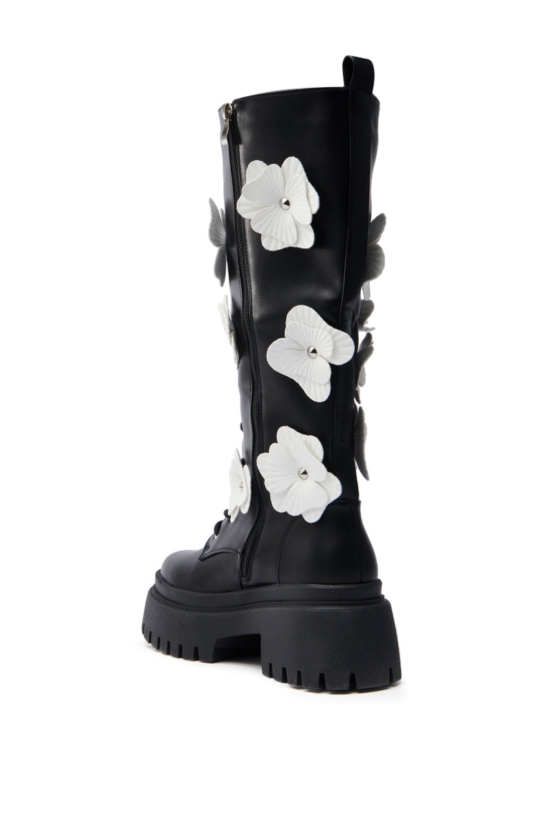 The AZALEA WANG MIRABELLA BLACK FLORAL EMBELLISHED BOOT features black knee-high faux leather boots with chunky soles, a side zipper, and large white and gray flower appliques, elegantly set against a plain white background.