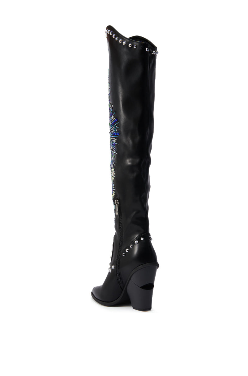 The AZALEA WANG AXELBEAT BLACK EMBELLISHED WESTERN BOOT is a single black, knee-high Western boot with a mid-high chunky heel, silver eyelets at the top and bottom, and blue and silver rhinestone designs on the outer side.