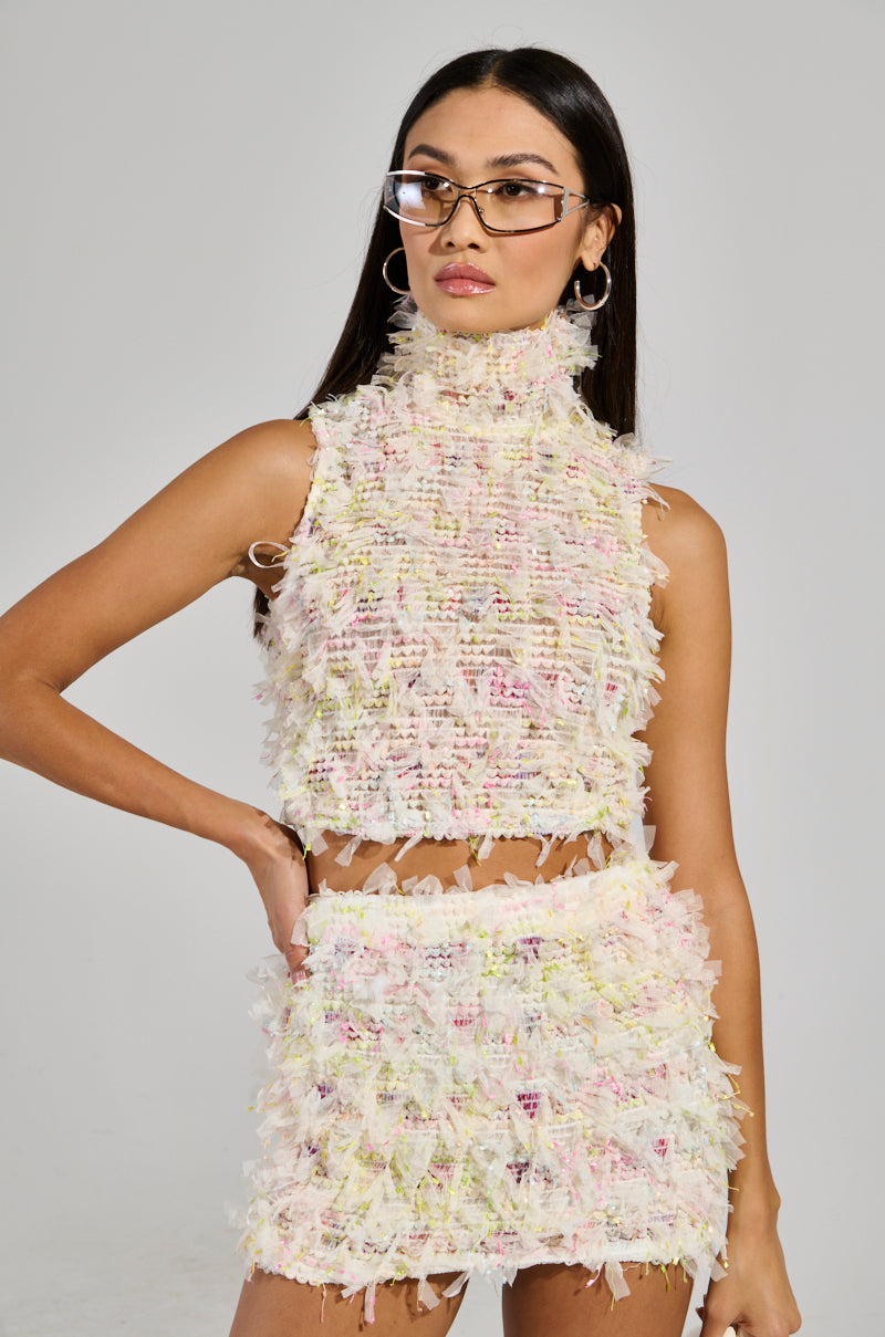 A woman with long hair wears the SWEET LIKE CANDY SLEEVELESS TOP paired with a matching pastel-colored high-neck skirt. Large sunglasses and hoop earrings accentuate her look as she poses confidently against a plain background.