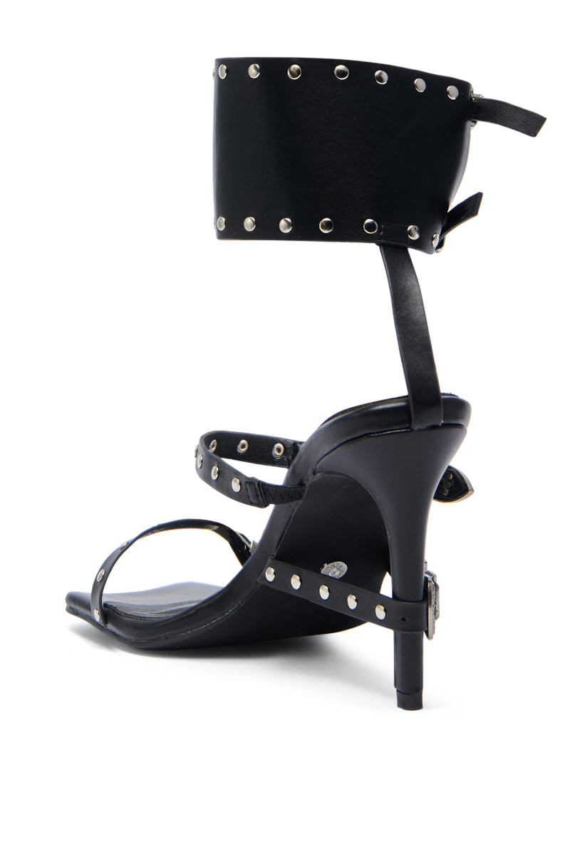 The AZALEA WANG AYBARS BLACK CUFFED SANDAL WITH WESTERN HARDWARE features sleek black leather, silver studs, a studded ankle cuff with wide buckle and tie closure, and a thin toe strap.