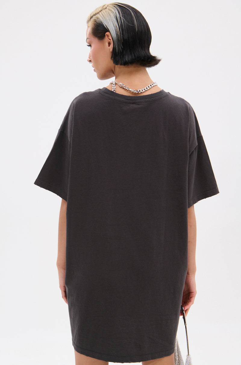 A person with short black hair and a bleached streak wears the oversized AALIYAH FOREVER GRAPHIC TSHIRT DRESS, facing away from the camera. Paired with a chain necklace and small bag, this look pays tribute to a true pop icon on a plain white background.